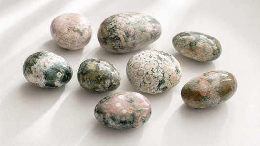 Sea jasper freeform crystals showing swirling green, cream, and pink orbicular patterns on a white surface
