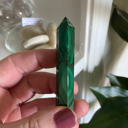 Hand holding a green malachite crystal tower against a blurred indoor background